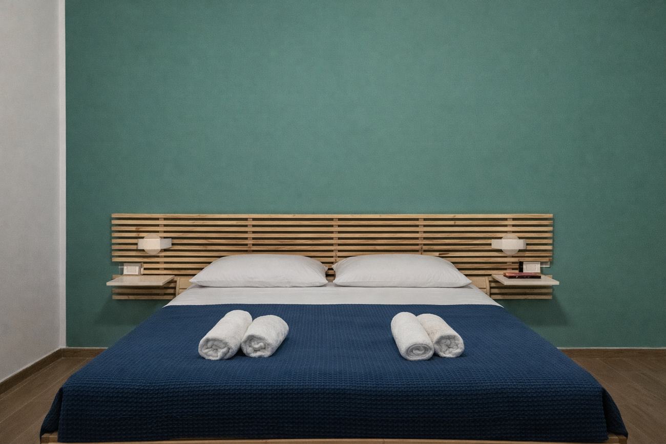 Camera con parete verde salvia, testata in doghe di legno e copriletto blu